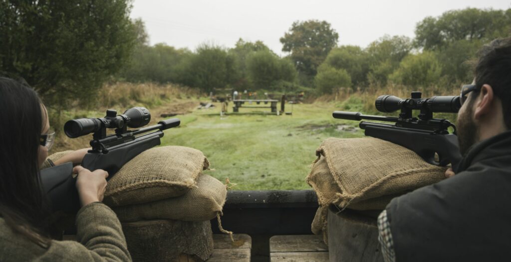 Man and woman aim air rifles at targets in the distance during spring break in the uk